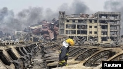 A firefighter walks among damaged vehicles as smoke rises amidst shipping containers at the site of explosions, at Binhai new district in Tianjin, China, Aug. 14, 2015.
一名消防员在烧毁的车辆中行走(2015年8月14日)。