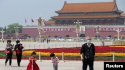 戴着口罩的北京市民在天安门广场为五一劳动节建起的花坛旁散步。(2020年4月29日)