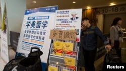 资料照片:在香港亚洲国际博览馆,一名来自中国的学生在参加完SAT考试后,在海外教育广告横幅后用手机通话。(2013年11月2日)