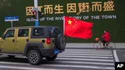 中国武汉街头一辆插着中国国旗的汽车从一名戴着口罩骑车的妇女身边驶过。(2020年1月29日)