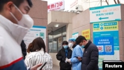 一名身穿防护服的医护人员在北京一家医院的核酸测试点外向民众讲解防护知识。(2020年12月28日)