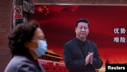 资料照:一名戴口罩妇女从习近平画像前走过。