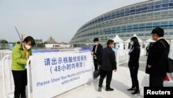 2021年10月8日,在中国国家速滑馆举行的冬奥会测试赛门外,工作人员引导人们出示新冠核酸检测结果。