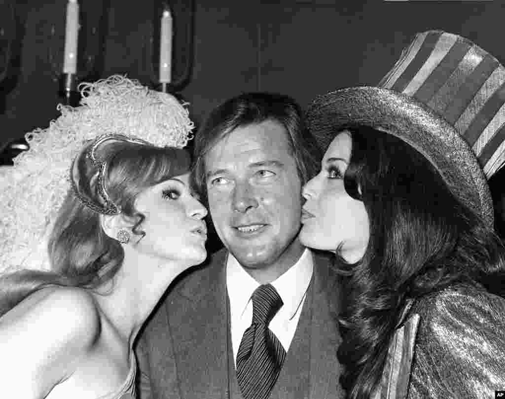 影星罗杰·摩尔1971年在世界小姐选美的午餐会上接受英国小姐和美国小姐的亲吻。 罗杰·摩尔的家人2017年5月23日说,他在和癌症短期搏斗后去世。  