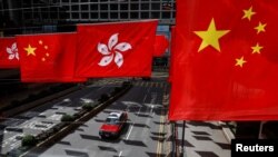 一辆出租车行驶在香港街道,一旁的购物中心外悬挂了香港旗帜和中国国旗。(路透社,2023年7月5日)