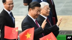 资料照:中共总书记、中国国家主席习近平与越共总书记阮富仲向举着中越国旗的欢迎人士挥手致意。(2017年11月12日)