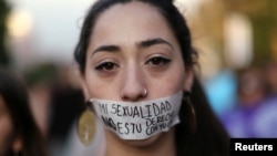 在智利圣地亚哥举行的声援“消除对妇女暴力国际日”的示威活动中,一名妇女用一块胶带把嘴封住,胶带上面写着“我的性别不等于你的配偶同居权。” (2016年11月25日)