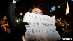 2024年12月4日,韩国总统尹锡烈宣布戒严后,人们聚集在首尔国会大厦,一个人举着一块写着“民主不会向尹锡烈屈服”字样的标语牌。