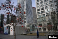 2020年2月18日星期二,只见一位戴口罩的女性在北京市中心商业区一座商业大楼前走过。