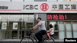 中国工商银行在北京的一家门市部门前,有提示“防抢劫”,一名男子带着女儿骑自行车经过(2013年6月26日)。