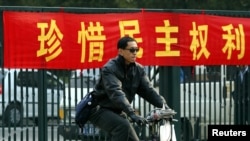 资料照:一名男子在北京街头骑车路过一条敦促市民”珍惜民主权利“的标语横幅。(2003年11月4日)