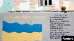 俄罗斯军人在克里米亚国际机场的一堵墙后面站岗,墙上画着乌克兰国旗,写着乌克兰国歌歌词