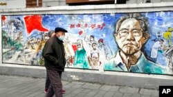 资料照片:在中国中部城市武汉封城76天纪念日前夕,戴着口罩的居民走过一幅名为“记忆”的壁画,武汉是首次发现冠状病毒的地方。(2021年1月22日)