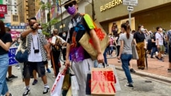 香港异见艺术家黄国才2020年7月1日,香港国安法实施第一日,在铜锣湾以”血拼”为名,打扮成来自中国大陆的”豪客”,手持多个写上国安法相关罪名的百货公司购物袋,表现对实施国安法的不安 (美国之音/汤惠芸)