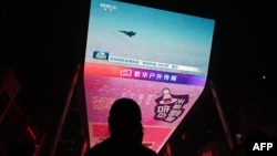 2024年10月14日,一名男子在北京一家购物中心外的巨型屏幕上观看有关中国在台湾周边进行军事演习的新闻节目。