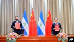 在这张中国官方新华社发布的照片中,尼加拉瓜总统丹尼尔·奥尔特加的儿子兼顾问雷亚诺·奥尔特加-穆里略和中国外交部副部长马朝旭展示他们共同签署的关于恢复外交关系的公报。(资料照片:2021年12月10日)
