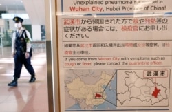 日本东京羽田机场一名戴着口罩的警察走过武汉肺炎的防疫广告牌。(2020年1月20日)