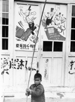 历史照片:在上海,一名男孩拿着竹竿在“绞死刘少奇”的宣传画前嬉戏。(1967年5月27日)