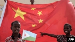 一名手举吉布提国旗的男孩站在中国国旗前等待参加中国资助的住房建设项目启动仪式(法新社2018年7月4日)
