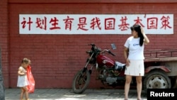 资料照:一个妈妈和孩子在“计划生育是我国基本国策”的标语前走过。(2002年7月23日)