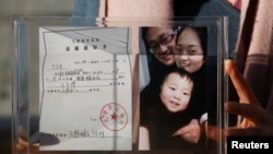 资料照:中国维权律师王全璋的妻子李文足手举全家福照片和天津警方的逮捕通知书。(2018年12月17日)