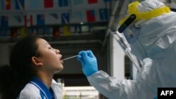资料照片:一位医务工作者用棉棒从一个学生口中获取样本进行新冠病毒核酸检测。