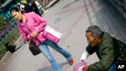 中国广州,一位女士从一个乞丐前面漠然走过。