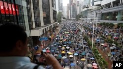 抗议者戴着口罩和打着雨伞游行在香港的一条街道上,一名男子在拍照。2019年10月6日, 美联社照片