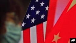 资料照片:中国外长王毅在外交部举行的“蓝厅论坛”上就中美关系发表演讲时,一名戴口罩的妇女坐在显示美中国旗的屏幕边。(2021年2月22日)