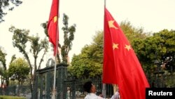 资料照:中越外长在河内举行会谈前,一名男子在越南政府办公机构前竖起的越南国旗旁升起中国国旗。(2017年11月2日)