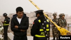 在中国新疆维吾尔自治区喀什的一条街上,警察检查一名男子的身份证,旁边有安全人员(2017年3月24日)