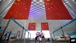 资料照:一名旅客推着行李车从深圳机场悬挂的中国国旗下走过。