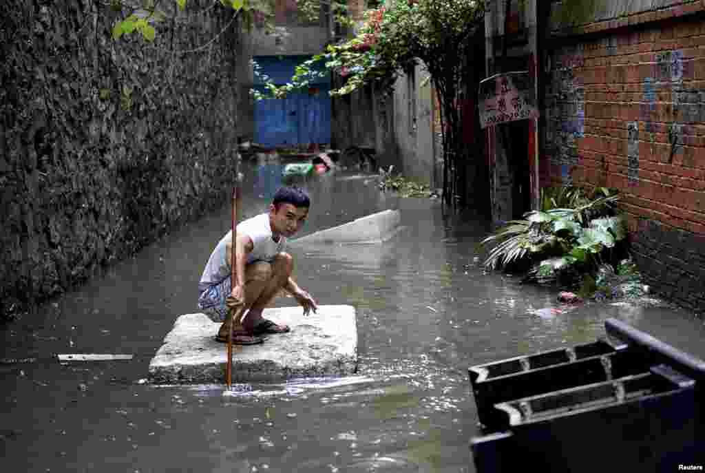2015年5月20日,广西柳州,强降雨让街上水流成河,有人蹲在发泡胶板上移动。