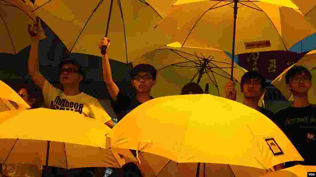 黄之峰(左二)和周永康(左)和其他人在集会上打开雨伞纪念占中满月(美国之音/伊万·布罗德黑德)