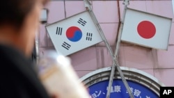 资料照:2019年8月2日,在东京新大久保地区的一家商店里,一名女子走过印有日本国旗和韩国国旗的广告(美联社)。