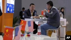 资料照:在上海举行的中国国际进口博览会期间,参观者在美国一家推广环境传感器公司的展位上在摆放着美中两国国旗的桌边谈话。(2019年11月6日)