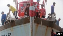 Migrant workers from Myanmar stand on a fishing boat as it arrives at the port in the southern Thai city of Pattani on June 18, 2014.