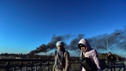 人们走过一座乌克兰西部城市利沃夫的一座立交桥,背后是从遭到俄罗斯导弹袭击的机场附近冒出的浓烟。(2022年3月18日)