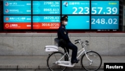 一名戴着口罩的日本警察骑车停站在东京街头一个日经指数电子显示板前。(2020年2月26日)