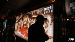 在北京街头一个公交车站一名男子走过显示中国志愿军参加朝鲜战争的电影“金刚川”的广告箱。(2020年10月22日)