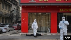 身穿防护服的中国卫生官员在检查一名在武汉一所医院附近倒地死亡的老年男子。(2020年1月30日)