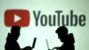 资料图:两位使用移动设备的人士站在YouTube图标投影前