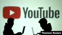 资料图:两位使用移动设备的人士站在YouTube图标投影前