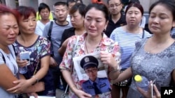 中国北部城市天津官员召开每日新闻发布会的宾馆外,一名女士拿着失踪的消防员儿子的照片。(2015年8月16日)