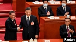 中国领导人习近平和新总理李强在全国人大会议期间握手,李克强在旁。(2023年3月11日)