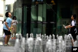 孩子们在北京街头的喷水池玩水。(2023年7月1日)