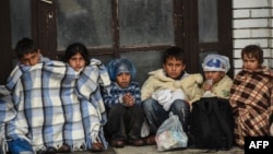 FILE - Children sit under covers as they wait with migrants and refugees near the registration camp in the town of Presevo after their arrival in Serbia, on Sept. 10, 2015.