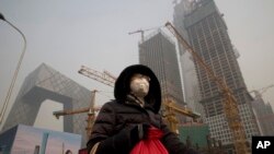 在雾霾中,行人戴口罩在北京中央商务区的央视大楼旁边的施工工地走过(1017年1月6日)