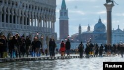 Orang-orang berjalan di Lapangan San Marko di Venesia Italia yang digenangi banjir hari Kamis (14/11).