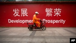 一名北京市清洁工人骑车经过市中心街头张贴的发展与繁荣的标语牌。(资料照片)